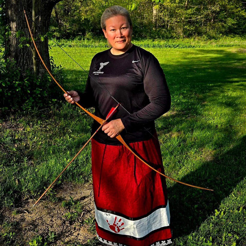 Cindy in a red ribbon dress with her bow and arrow displaying her archery expertise.